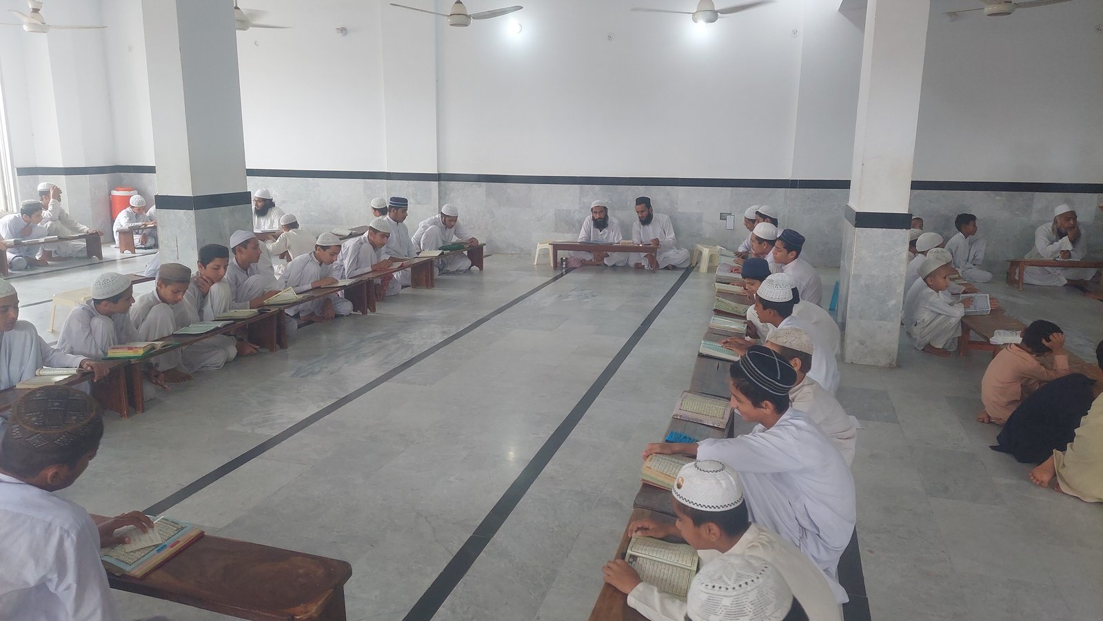 Students studying at low desks in the Madrassa learning hall