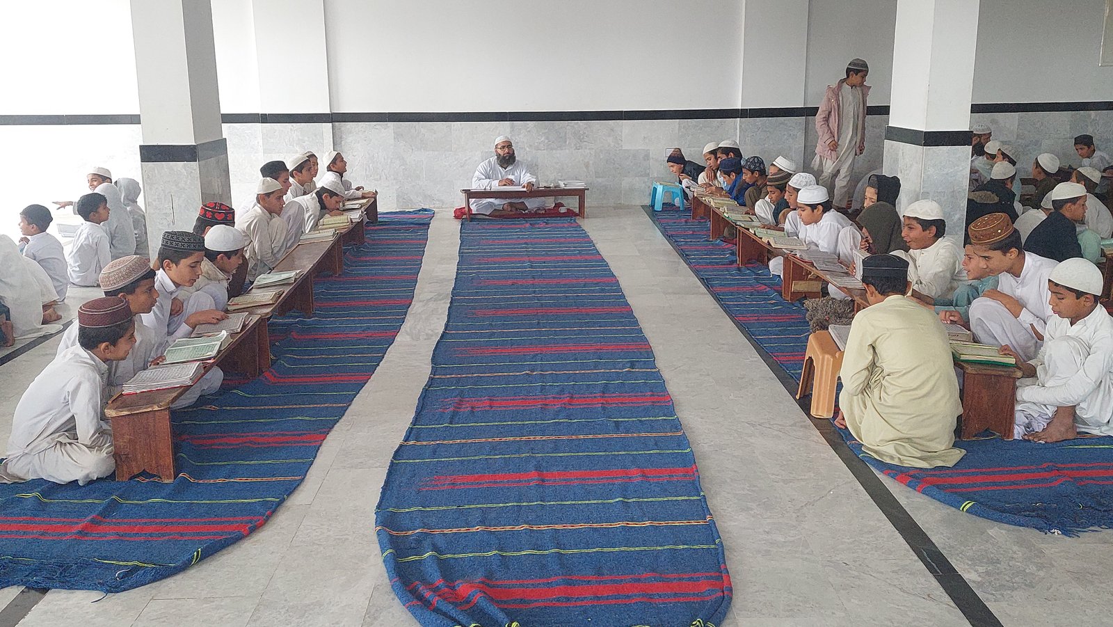 Students studying in rows with a teacher at the front of the Madrassa classroom