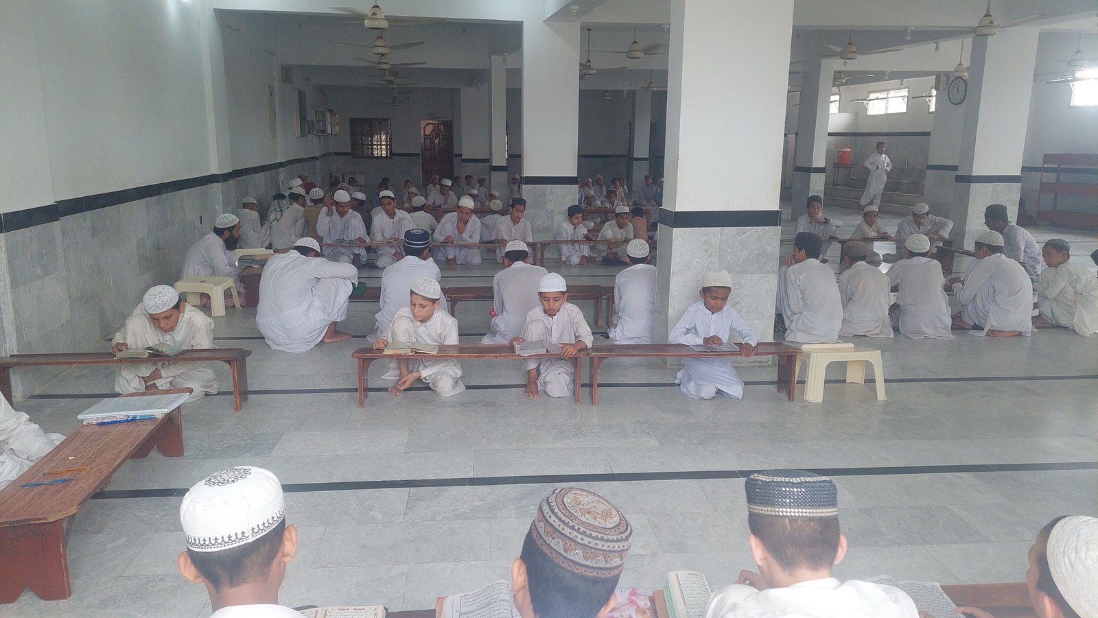 Students reading at low desks in a large Madrassa classroom